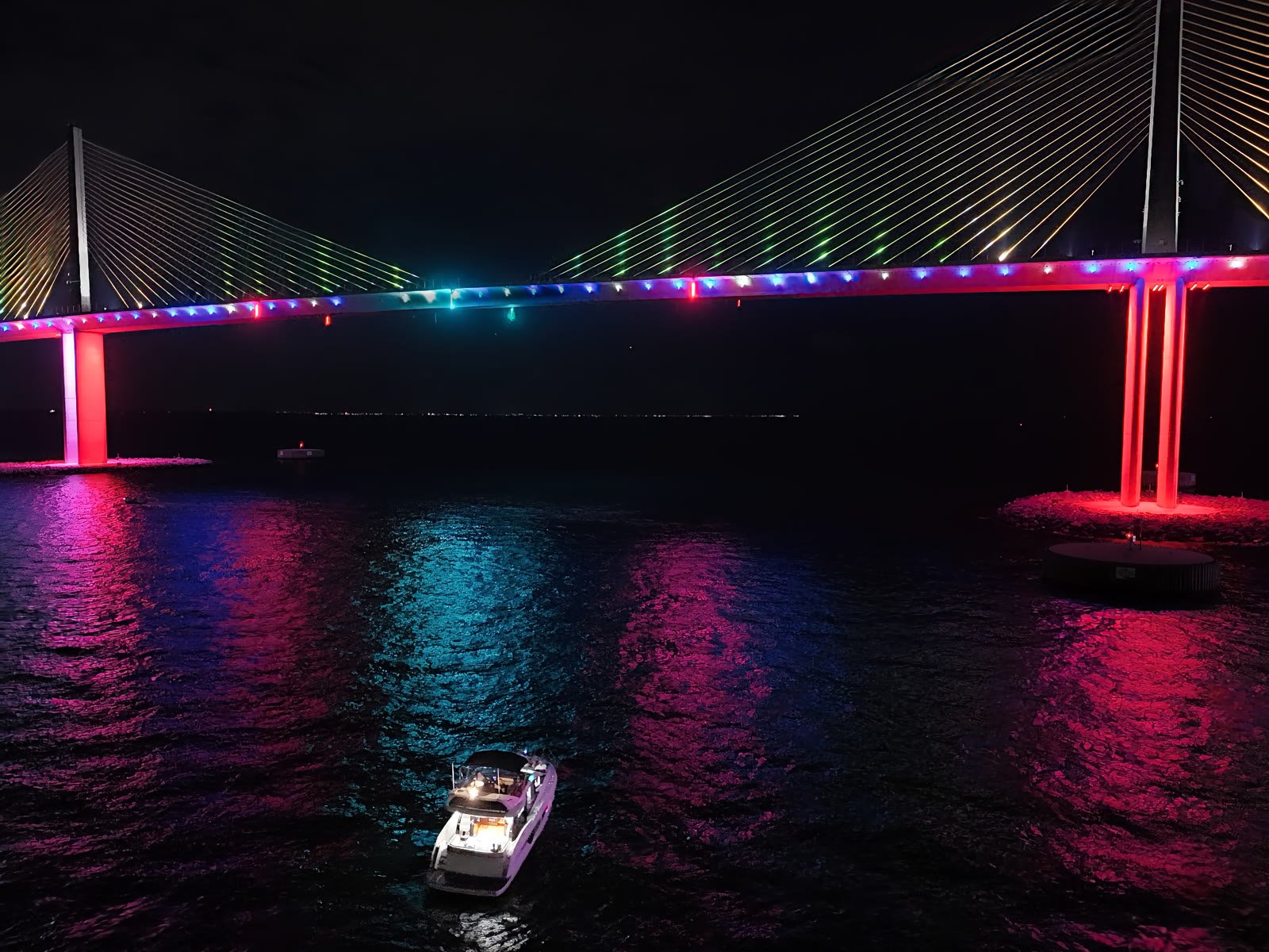 Good Vibes on the water at night beneath the Sunshine Skyway bridge lit in colour