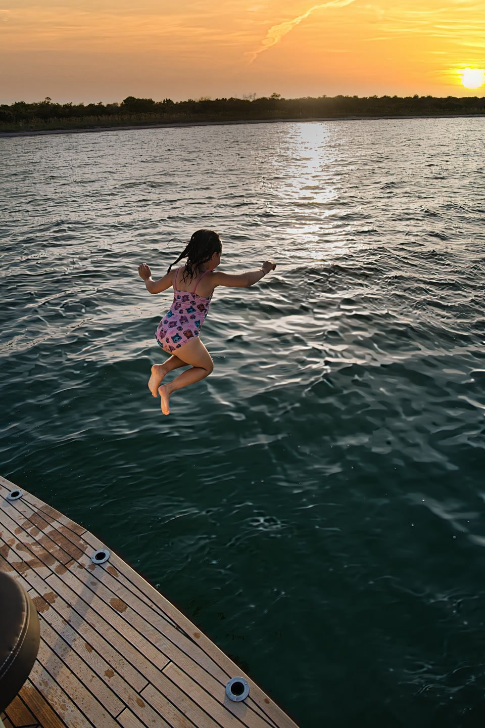 A child jumping from the teak swim platform into the water at sunset