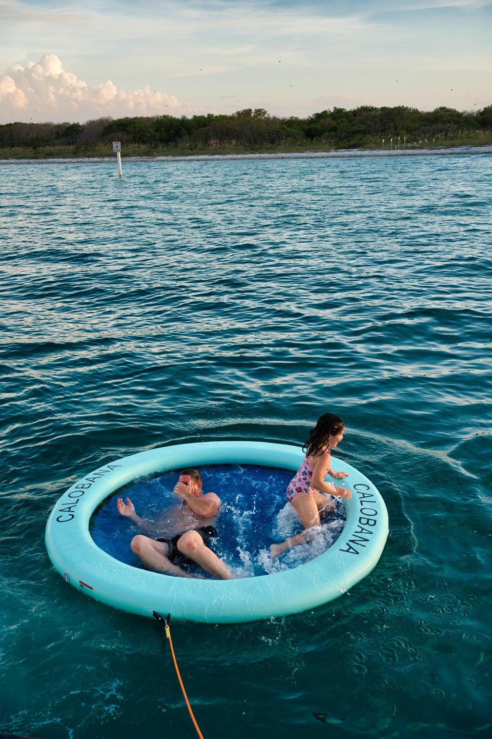 Two guests splashing in the floating pool ring beside the yacht